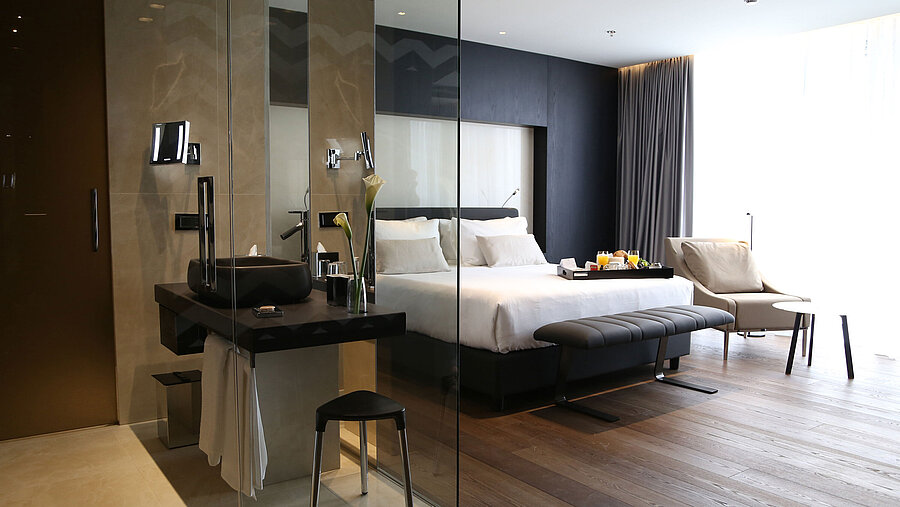 Habitación luminosa con cama doble, baño acristalado y zona de estar en el Maritim Hotel Plaza Tirana