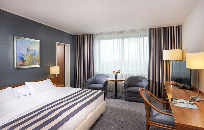 Habitación familiar en el Maritim Hotel Ulm con cama doble, escritorio, sillones y luz natural