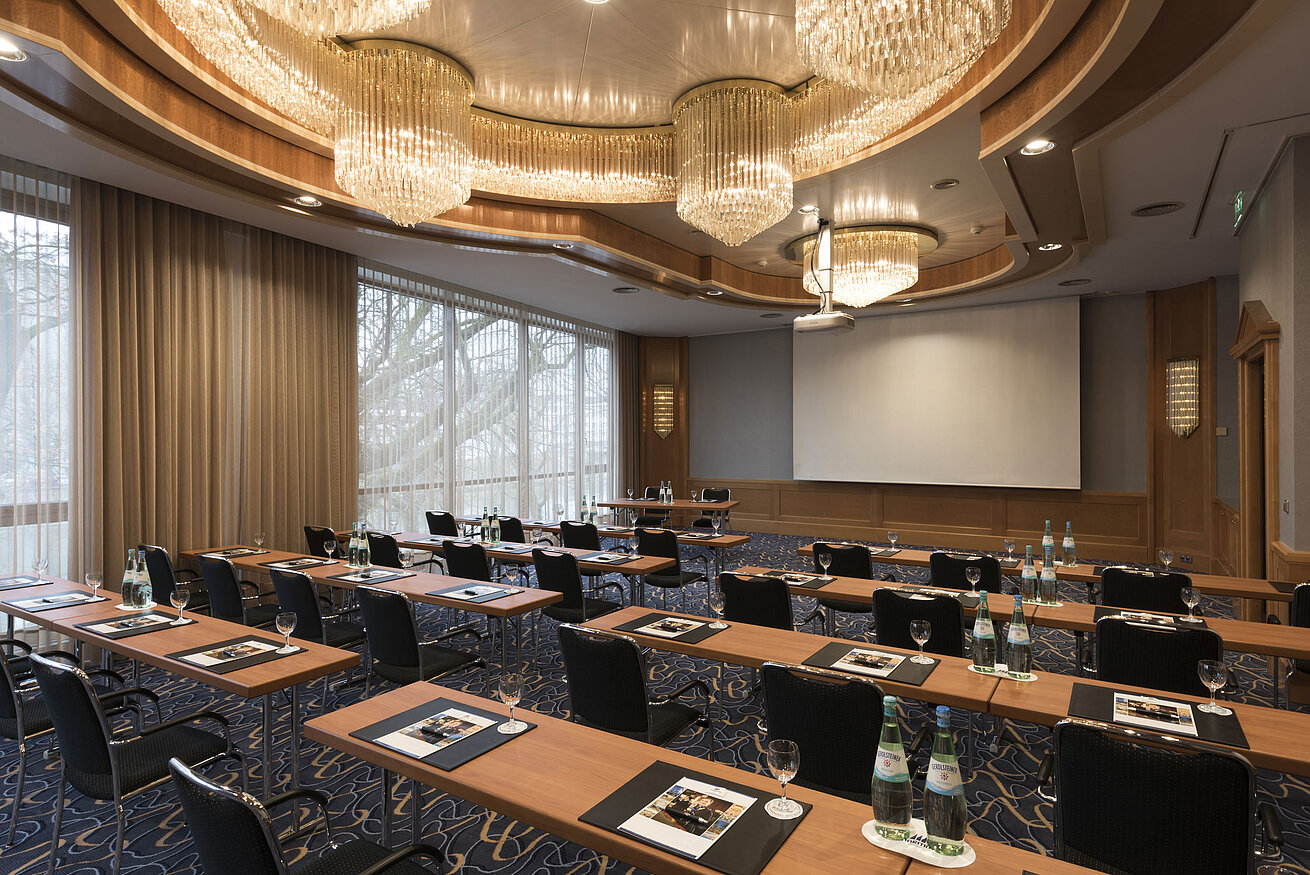 Sala de conferencias elegante con sillas en fila, lámparas y pantalla en el Maritim Hotel Ulm.